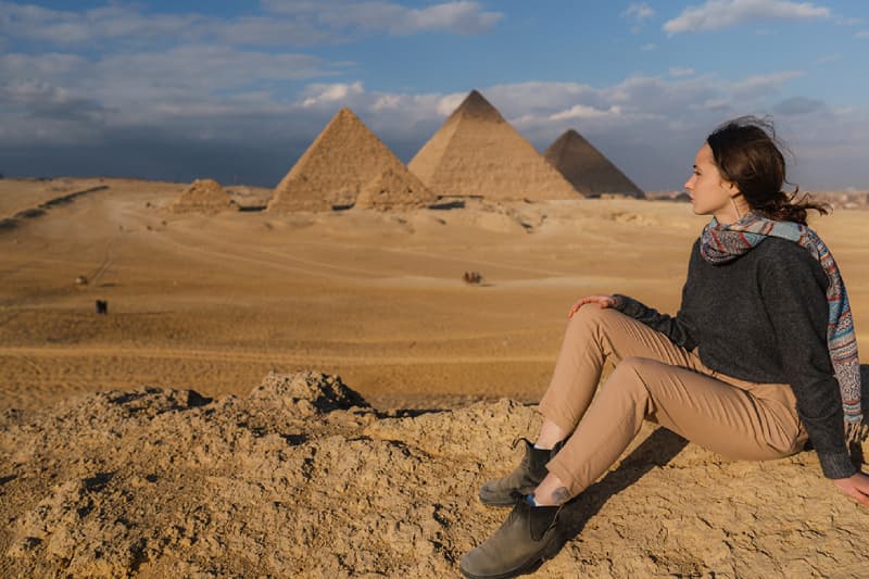 Faszinierende Aussicht auf die Pyramiden in Ägypten Frau sitzt in der Wüste mit Blick auf die Pyramiden von Gizeh
